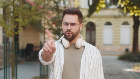 upset caucasian man reacting to unpleasant awful idea shaking finger at camera on city urban street