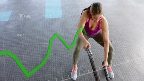 green line graph animation over woman exercising with battle ropes in gym