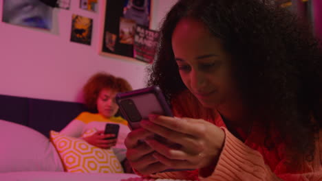 dos mujeres jóvenes usando teléfonos inteligentes en un dormitorio