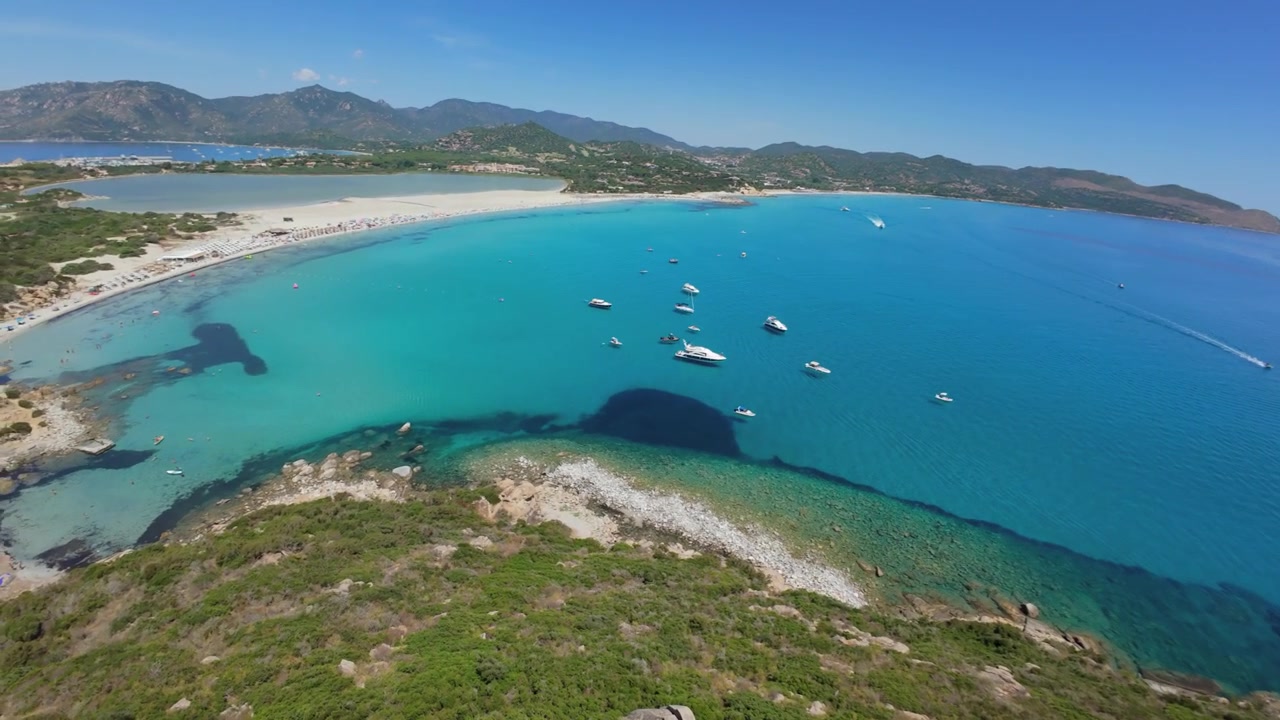 Drone che vola vicino sopra una torre di avvistamento bianca, poi giù per il fianco della collina verso il mare turchese, Villasimius, Sardegna. Riprese aeree FPV della costa mediterranea