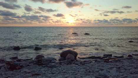 puesta de sol en una playa rocosa con olas golpeando la orilla