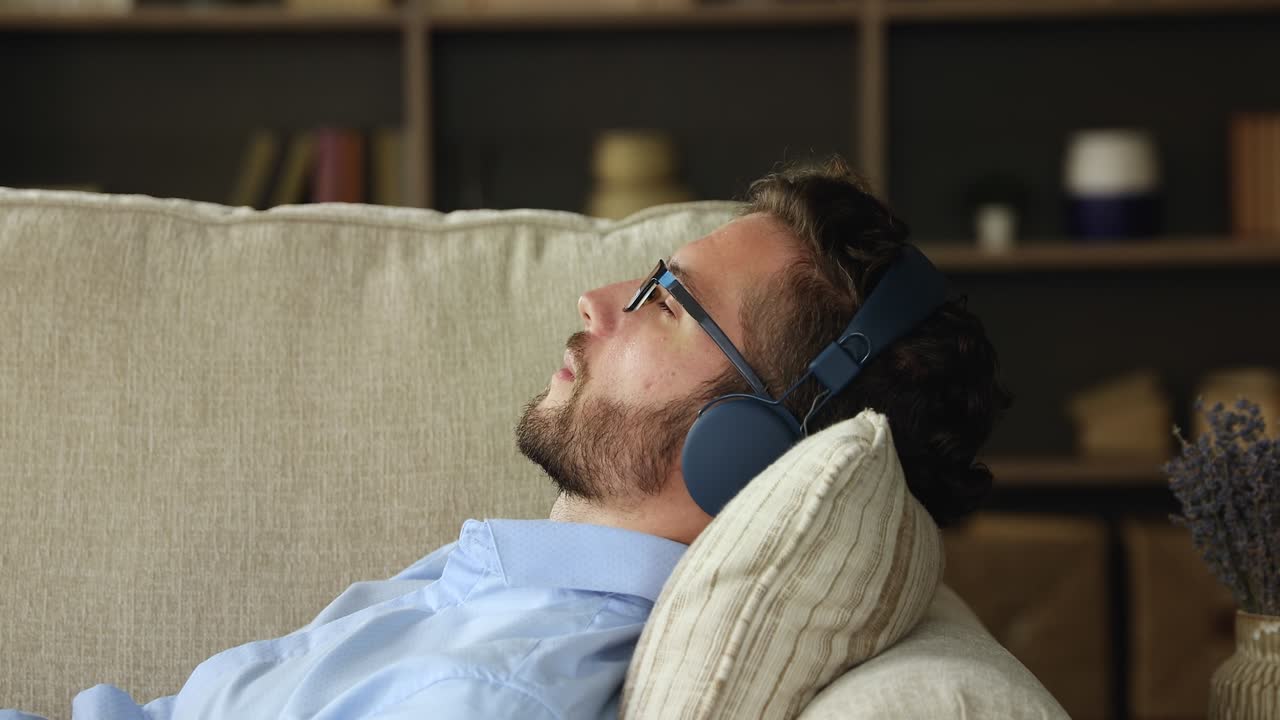Millennial male wear earphones lying on couch listening to music