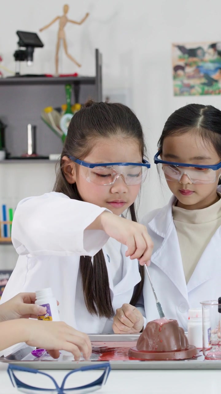 Anak-anak Asia mengenakan jas lab dan kacamata pelindung melakukan percobaan gunung berapi kimia di sekolah