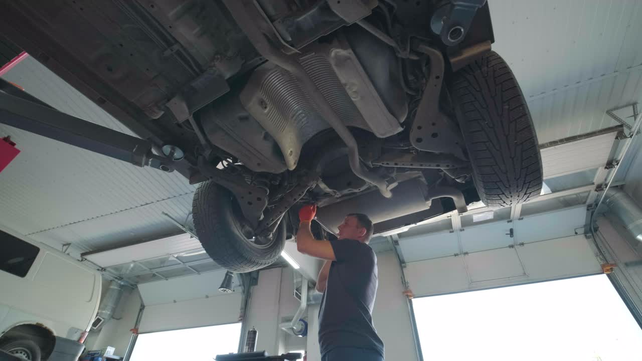 joven mecánico profesional que trabaja bajo el coche moderno levantado en el servicio de reparación de automóviles. servicio de automóviles, mantenimiento de reparación.