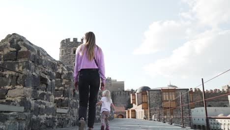 young mother with two little daughters climbing on a wall of medieval castle