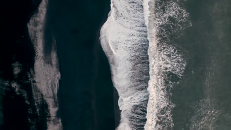 top view of waves splashing on black sand beach in vik, south iceland - drone shot