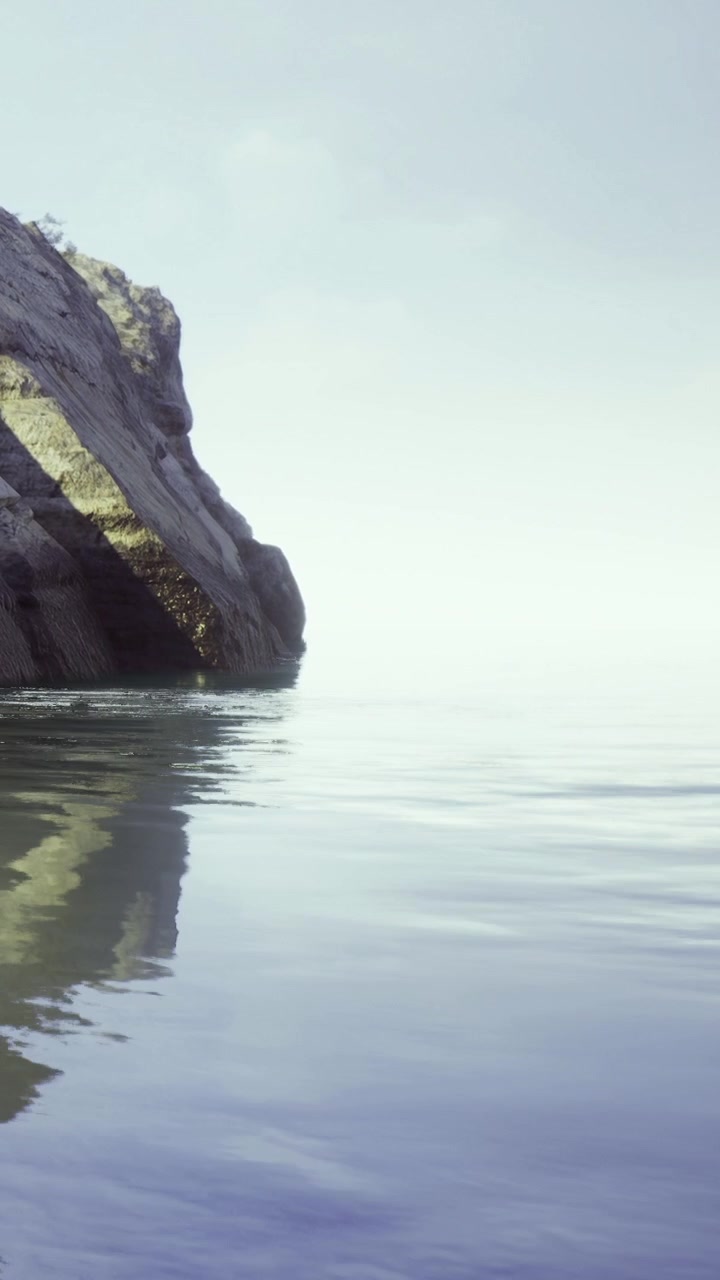 Sunrise over calm water at rocky shoreline with gentle wave reflections