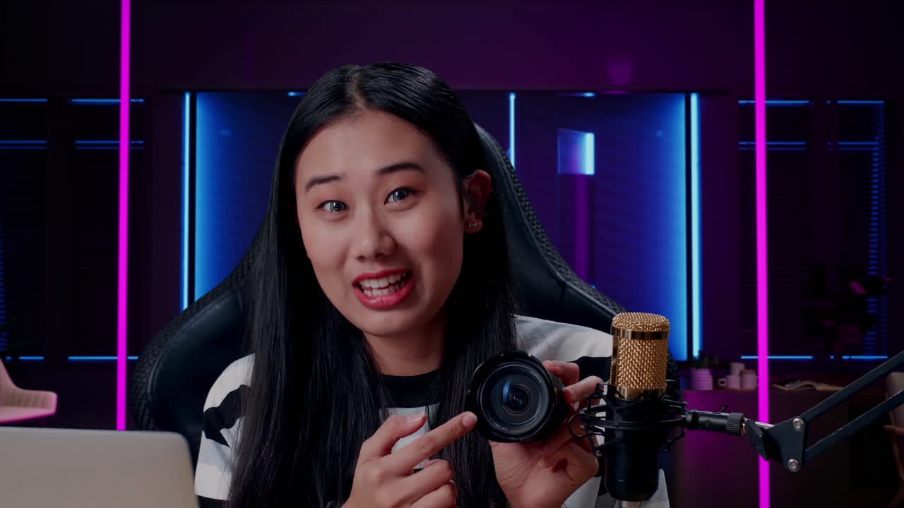 un primer plano de una mujer asiática sonriente con una cámara de revisión de computadora en una habitación iluminada por luces de neón en retro