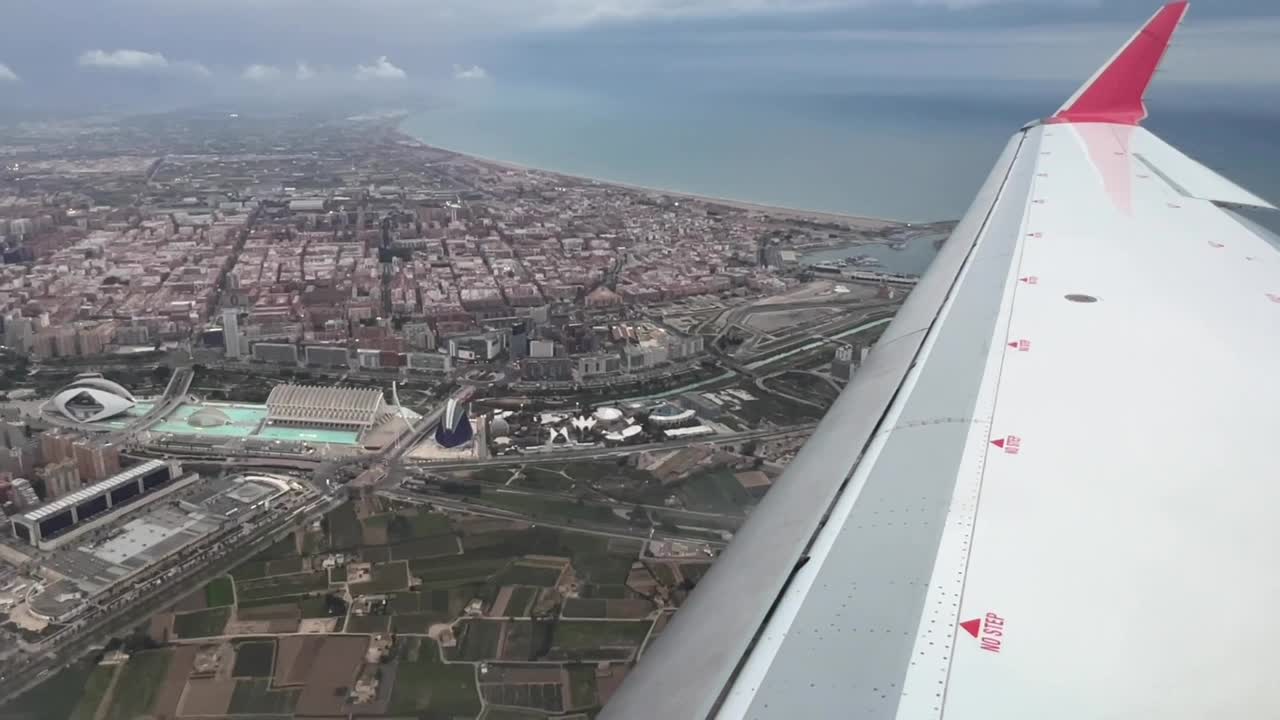 View of the right wing of a medium size jet approaching to land to Valencia’s airport, with a lateral view of Valencia city (Spain)  in a stormy Spring afternoon while configurating the plane