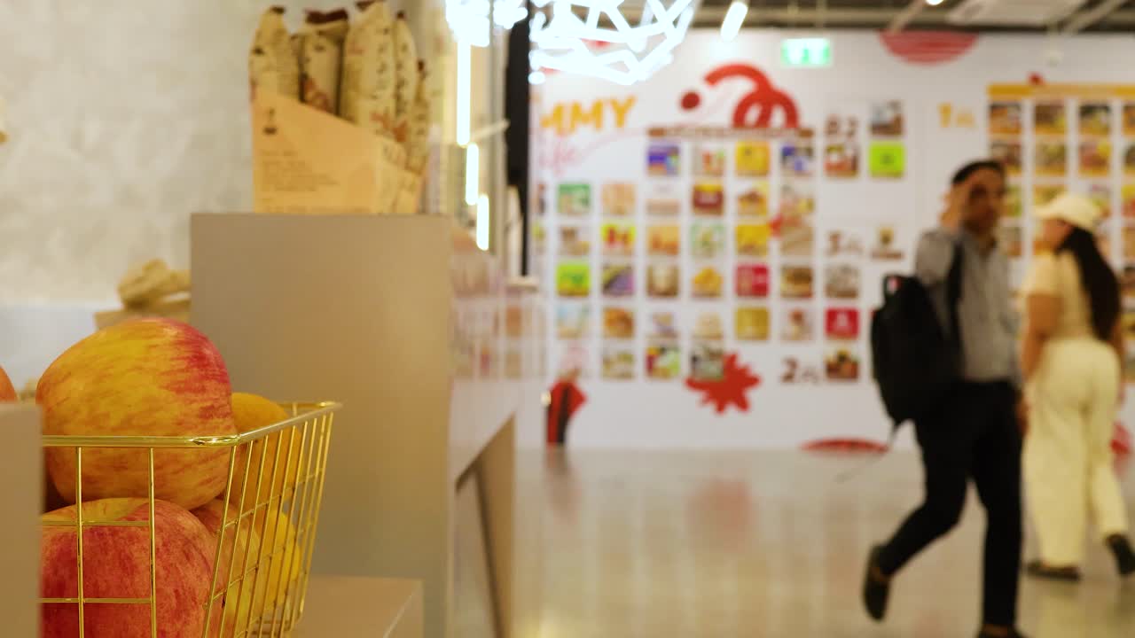 People walk past a vibrant fruit juice cafe with colorful decor and fresh produce in a bustling mall