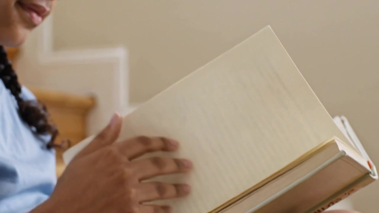 Bambino con una maglietta azzurra che apre un libro tascabile e sfoglia le pagine su scale di legno per studiare, con spazio per il testo.