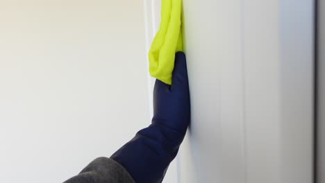 a gloved hand wipes down a white door frame with a yellow cloth.