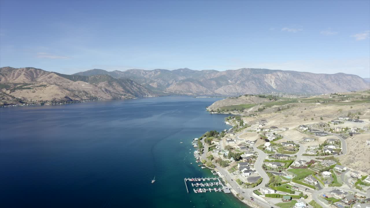 Drone flying over houses towards lake and mountains. 4k Lake Chelan aerial footage. Scenic mountains around lake. Beautiful lake drone footage.