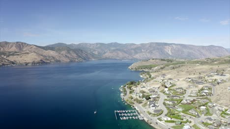 drone flying over houses towards lake and mountains. 4k lake chelan aerial footage. scenic mountains around lake. beautiful lake drone footage.