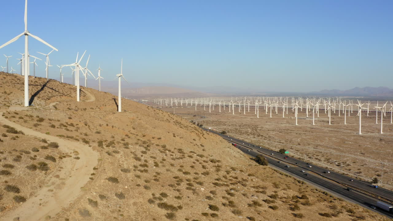 drone volando de lado con vistas a la carretera entre un enorme parque eólico y turbinas cerca de palm springs en el desierto de mojave, california, ee.uu.
