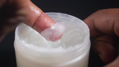 person applying white cream from a jar