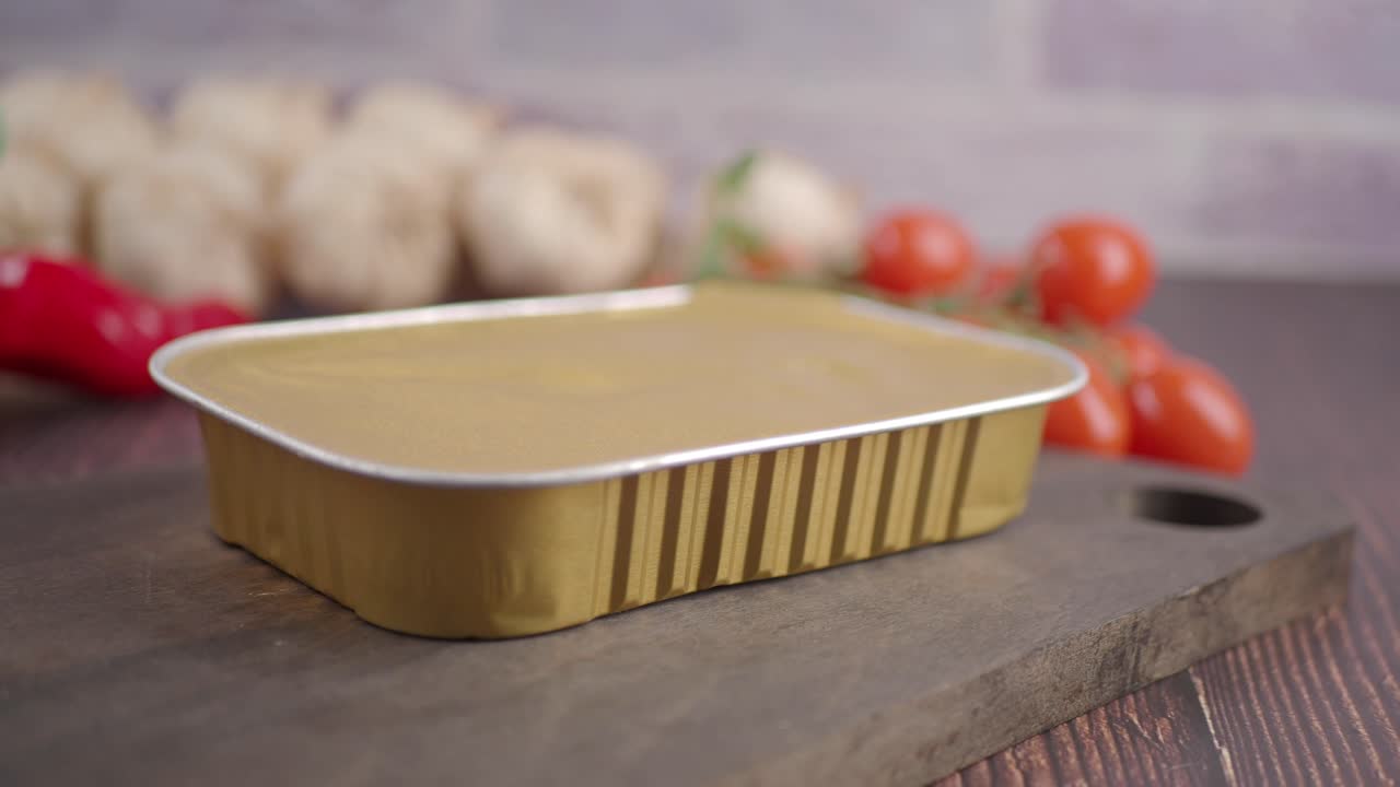 Contenitore per alimenti in lamina dorata su tavola di legno con verdure fresche
