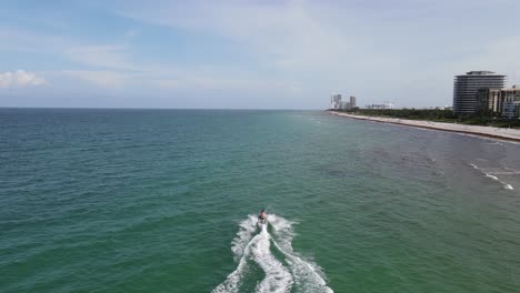 Aerial-follows-jet-skiers-enjoying-warm-sunny-day-on-sandy-beach,-Miami