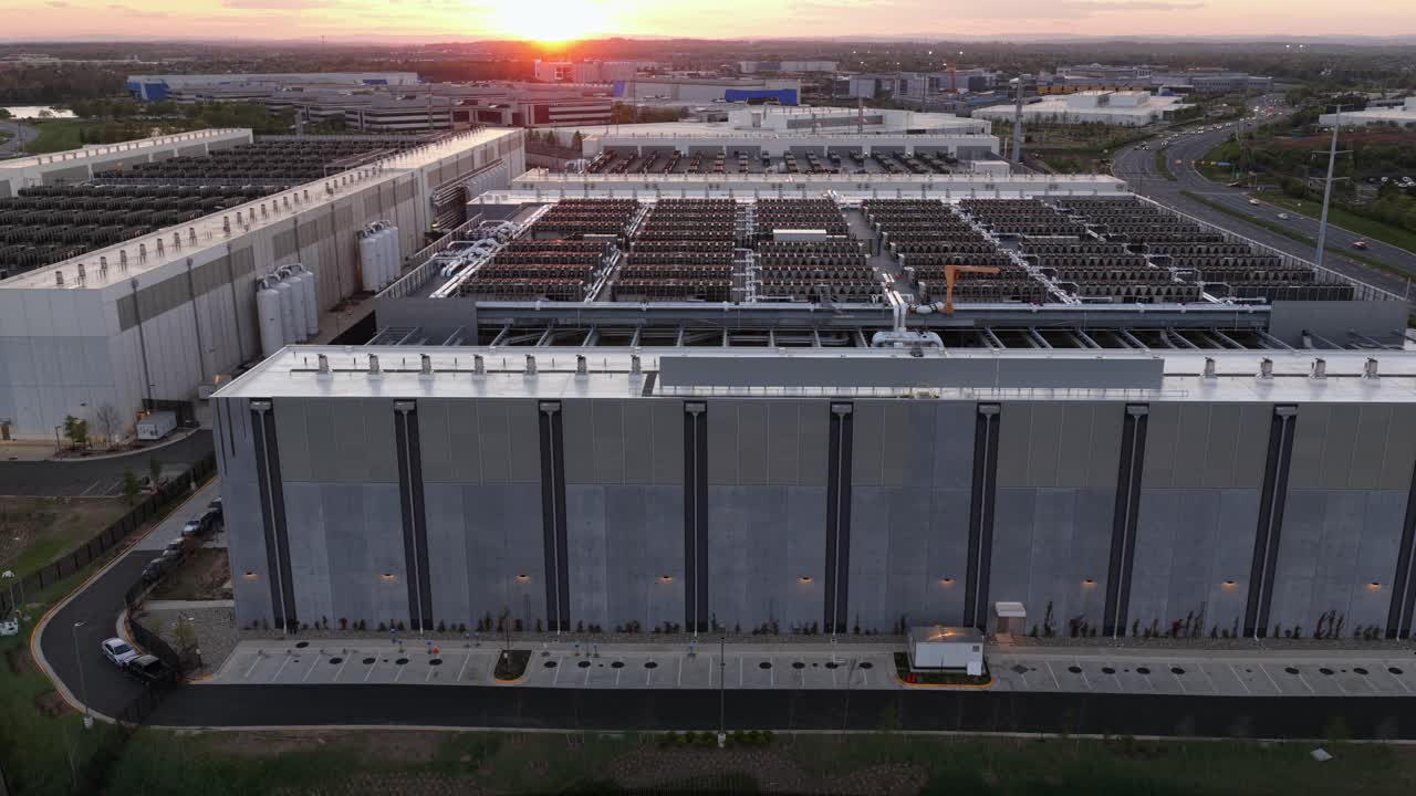 Stort datacenterkompleks i Ashburn, Virginia, USA ved solnedgang, der viser store serverbygninger, kølesystemer på taget og moderne cloud-infrastruktur nær Washington DC. Lateralt luftfoto.