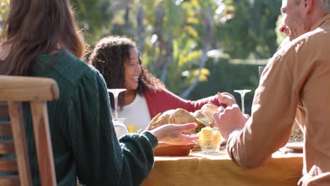 happy diverse male and female friends saying prayer on thanksgiving celebration meal in sunny garden