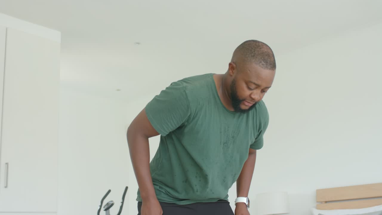 Man rising from bed and floor after bike workout, pushing up with hands, towel nearby, breathing