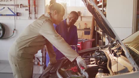 video of two diverse female car mechanics talking and repairing car