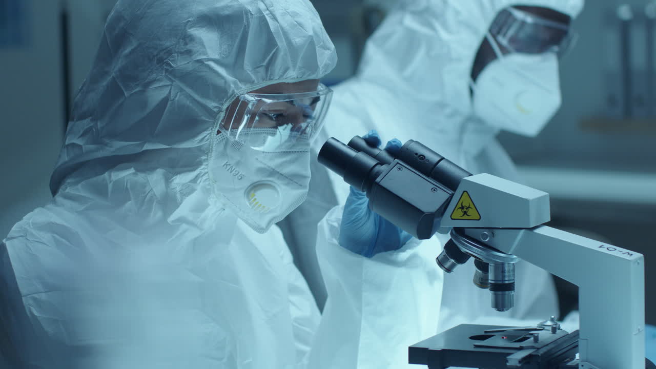 Female Lab Scientist in Protective Uniform Examining Blood under Microscope