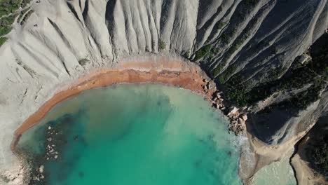 Vista-Giratoria-De-Arriba-Hacia-Abajo-De-Una-Playa-De-Arena-Tropical-Con-Agua-Turquesa-Clara,-Bahía-De-Qarraba-Y-Acantilados-De-Arcilla,-Malta