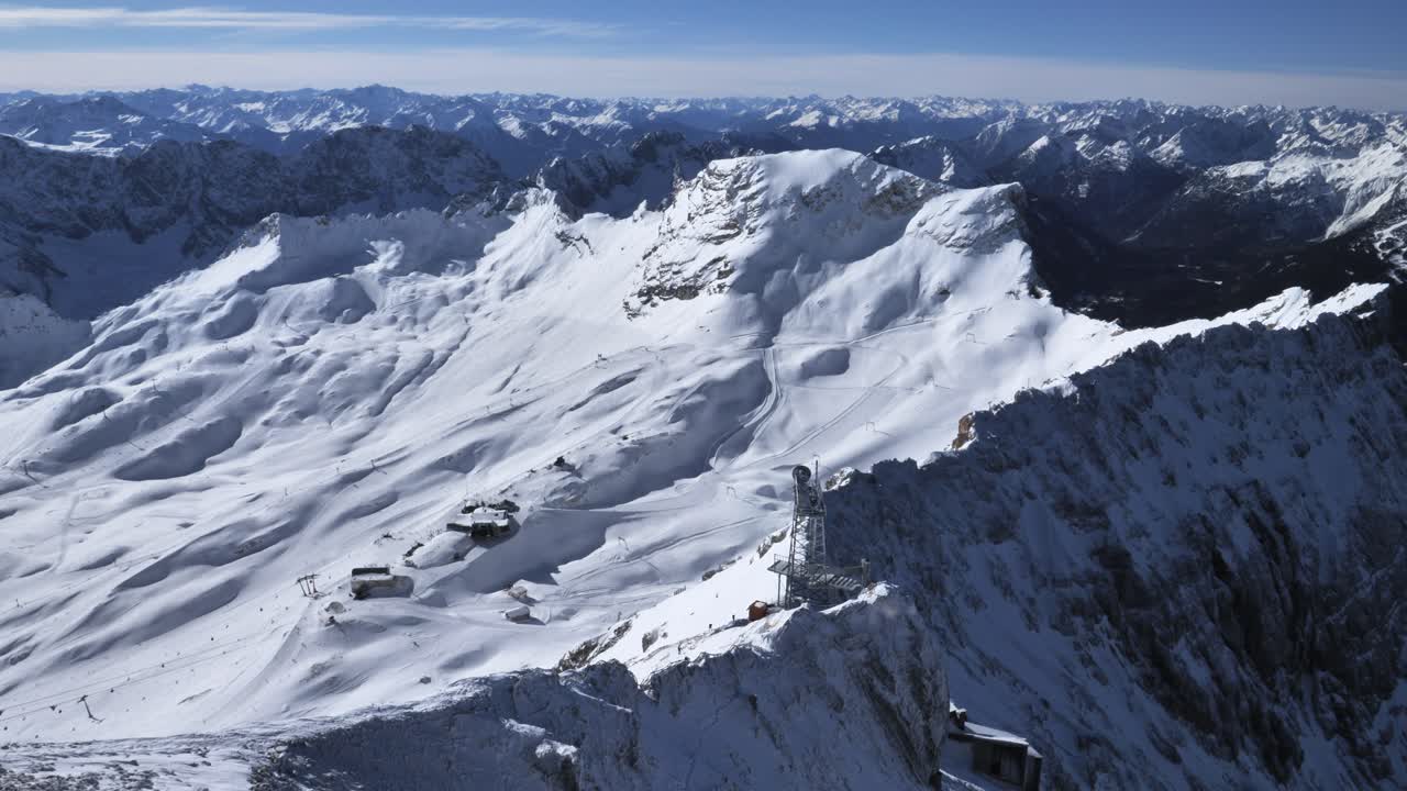 Vista di un ghiacciaio alpino innevato con stazione sciistica e impianti di risalita su un crinale ad alta quota sotto un cielo invernale limpido e azzurro.