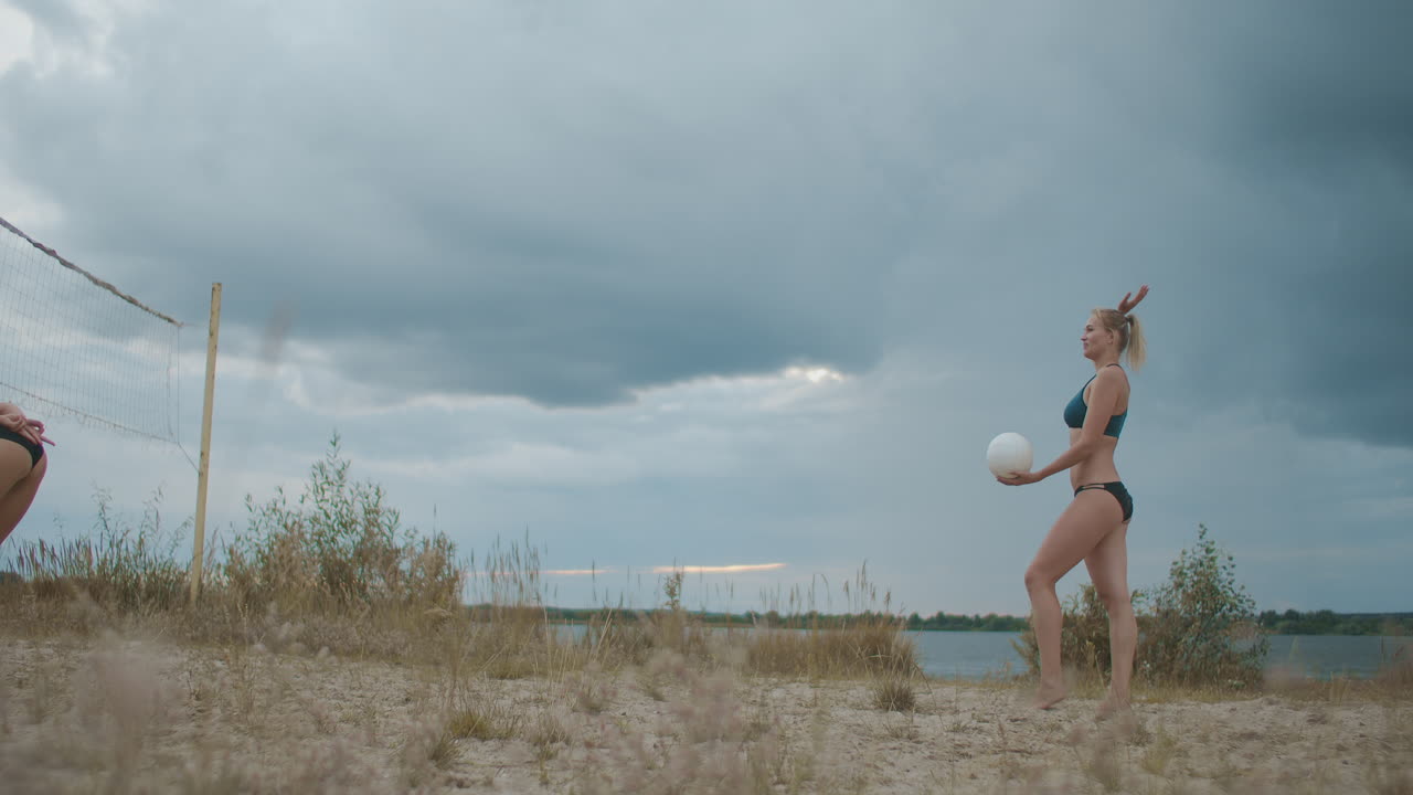 아름다운 여자들이 스포츠 비키니를 입고 여름 휴가 동안 비치 볼리볼을 하고 운동선수 여성들이 점프하고 있습니다.