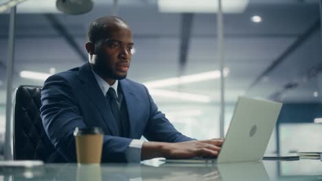 top management modern office: successful black businessman in tailored suit working on laptop computer. professional african american ceo managing stock markted investment clients accounts