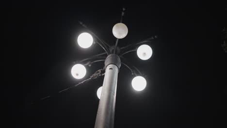 vista de cerca de un poste de farola con cinco bombillas iluminadas contra un cielo oscuro