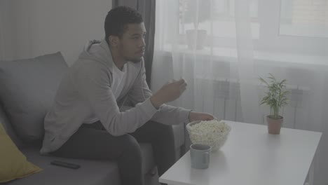 young african american man watching attentively a movie and eating popcorn