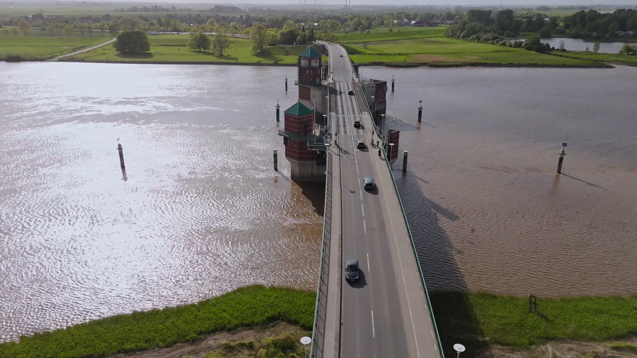 Aerial drone shot of the Jann-Berghaus bridge near Leer, Germany. The clip shows traffic over the Ems River, a movable span, and the surrounding rural landscape from a high-angle perspective.