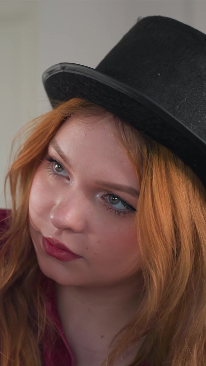 Subjekt viditelný od ramen nahoru ukazující pohyb hlavy. Viditelné oblečení ukazuje možný červený oděv na úrovni krku. Osvětlení vytváří jasný pohled na vlasy, klobouk a horní část těla.