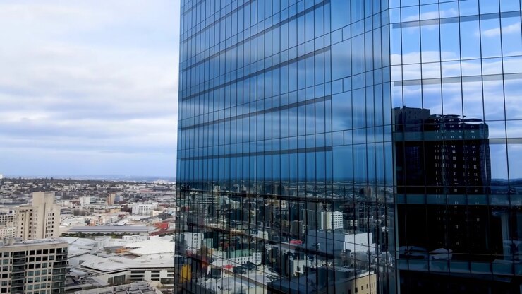 Grattacielo di vetro che riflette lo skyline della città, vista aerea della facciata a specchio e delle torri vicine che dominano.