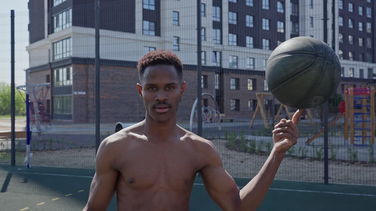 Afroamerikansk mand uden trøje spinder basketball på fingeren på en bane