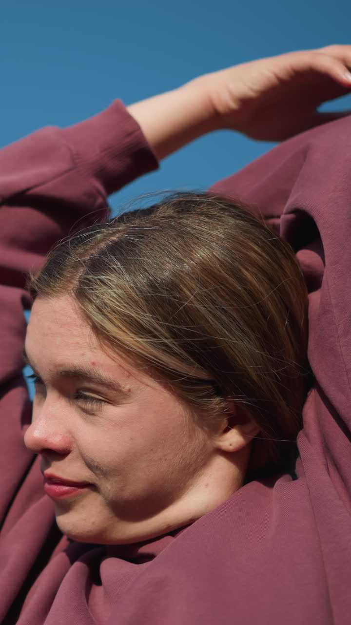 은 하늘 아래 빛이 그녀의 얼굴을 강조하는 동안 따뜻한 미소로 피트니스 운동에 참여하는 운동선수, 머리 위에 팔을 펴고, 그녀는 집중하고 편안해 보입니다.