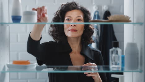 View-Through-Bathroom-Cabinet-Of-Mature-Woman-Getting-Ready-And-Putting-In-Earrings