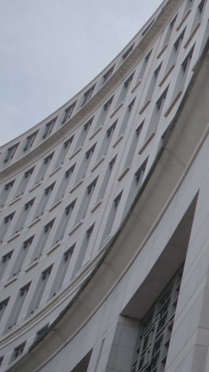 Curved modern building facade in London, shot vertically with cloudy sky