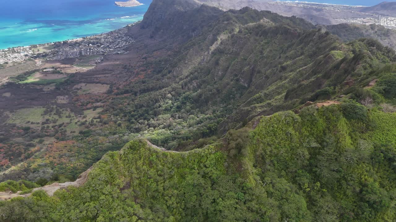 Filmagem cinematográfica com drone sobre os picos de altas montanhas em Oahu, Havaí, com o litoral oceânico à distância. Montanhas tropicais dramáticas e litoral da ilha panorâmico