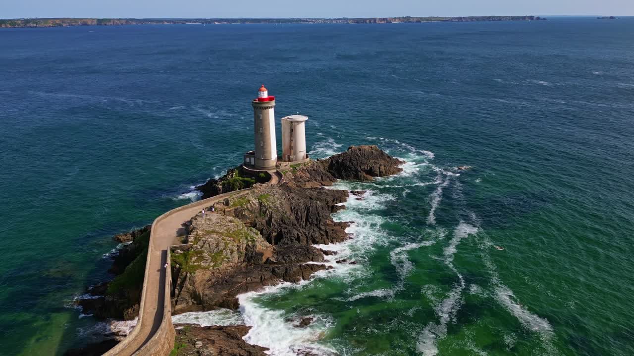 Drone in downward motion follows the stone path to Petit Minou lighthouse. Waves crash around the rocks and the sea stretches to the horizon - Brittany, France