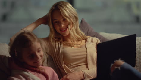 Mom-with-laptop-chatting-with-daughter-at-home.-Mother-touching-girl-face-couch