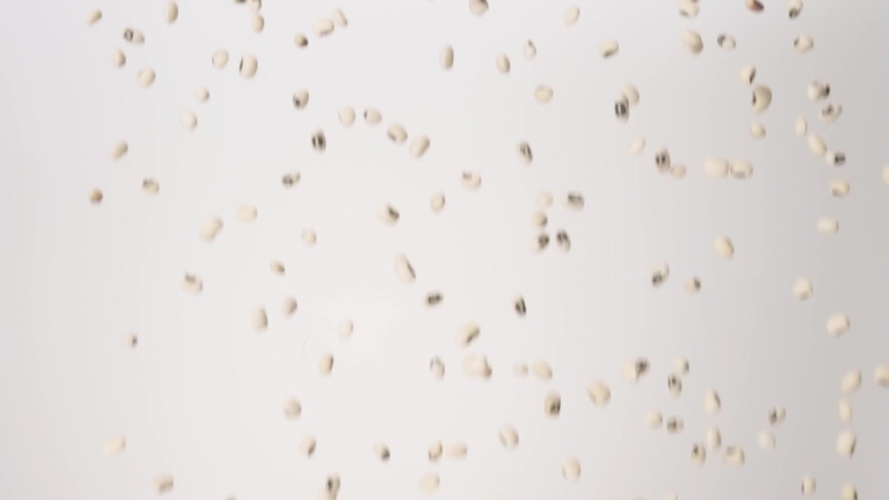 Fagioli dall'occhio nero portafortuna del Capodanno del Sud che cadono su uno sfondo bianco in slow motion, primo piano macro