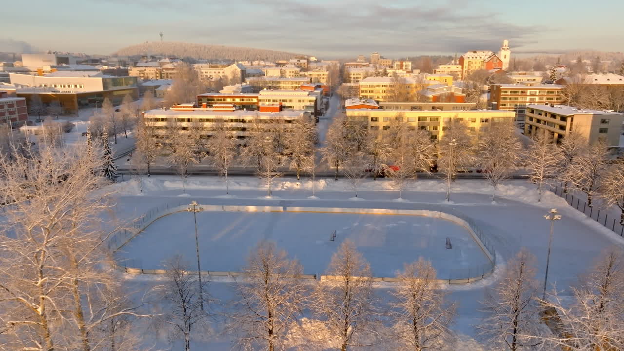 Aerial view around a ice hockey rink, tilting toward the city, sunrise in Kuopio