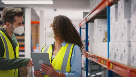 Workers-In-Warehouse-Training-Male-Intern-Standing-By-Shelves-All-Wearing-Face-Masks