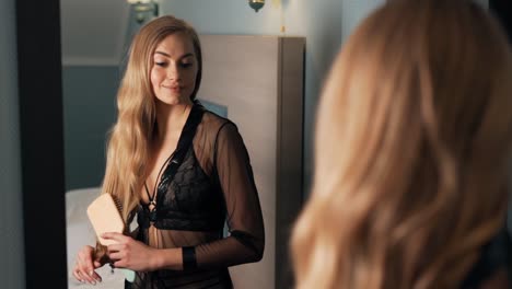 Pretty-young-woman-combs-her-hair-with-a-wooden-brush-standing-in-front-of-a-mirror