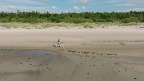 aerial view with a young longhaired girl riding a bike on the sandy beach, sunny day, white sand beach, active lifestyle concept, wide drone dolly shot moving right, slow zoom in