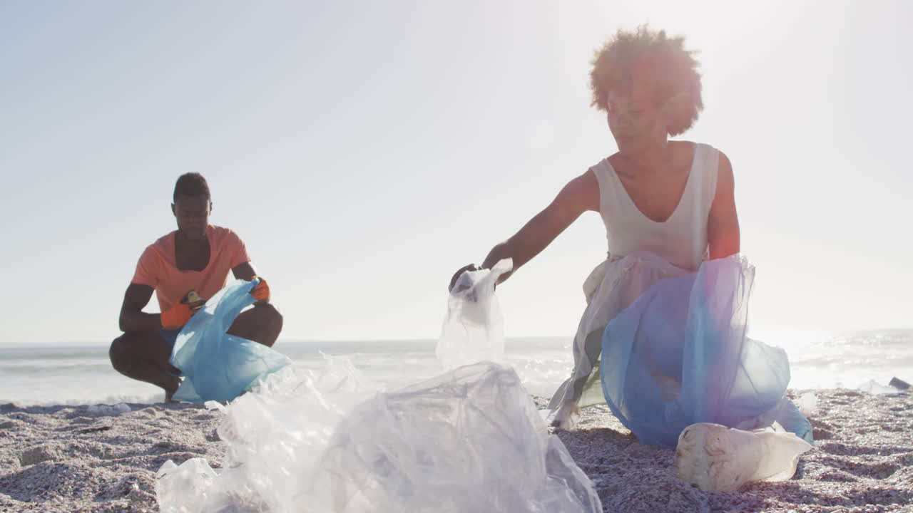 Coppia afroamericana che differenzia i rifiuti insieme su una spiaggia sporca e soleggiata