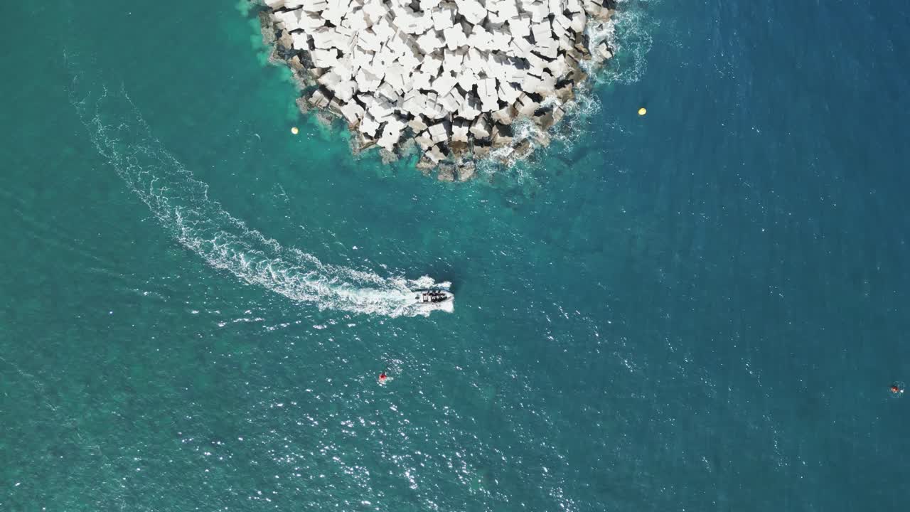 Boat exits port harbor rounding corner of large breakwater, drone top down bird's eye view static